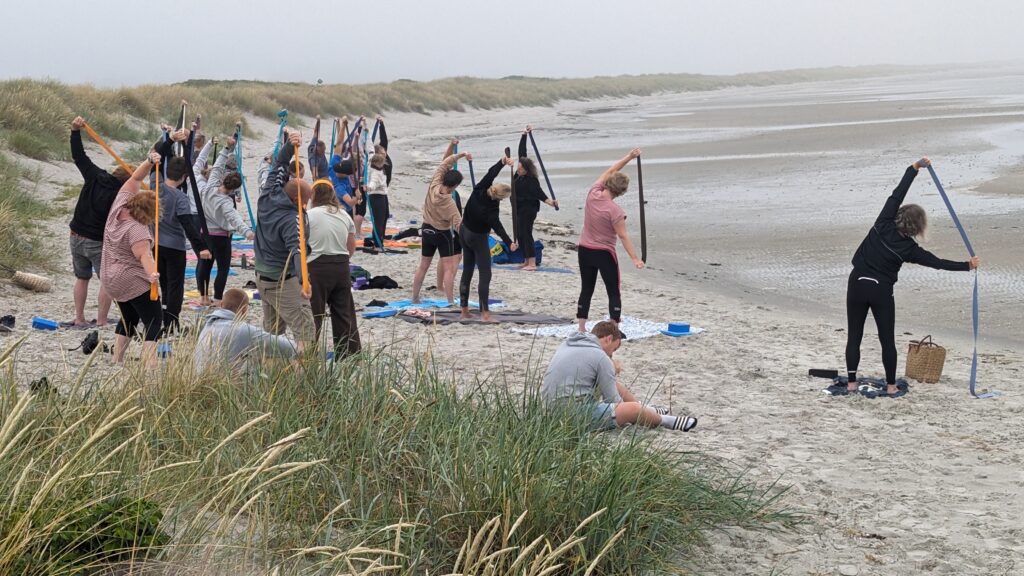 Der dyrkes Yoga med stropper på stranden i Hou. To af deltagerne tager en siddende pause.