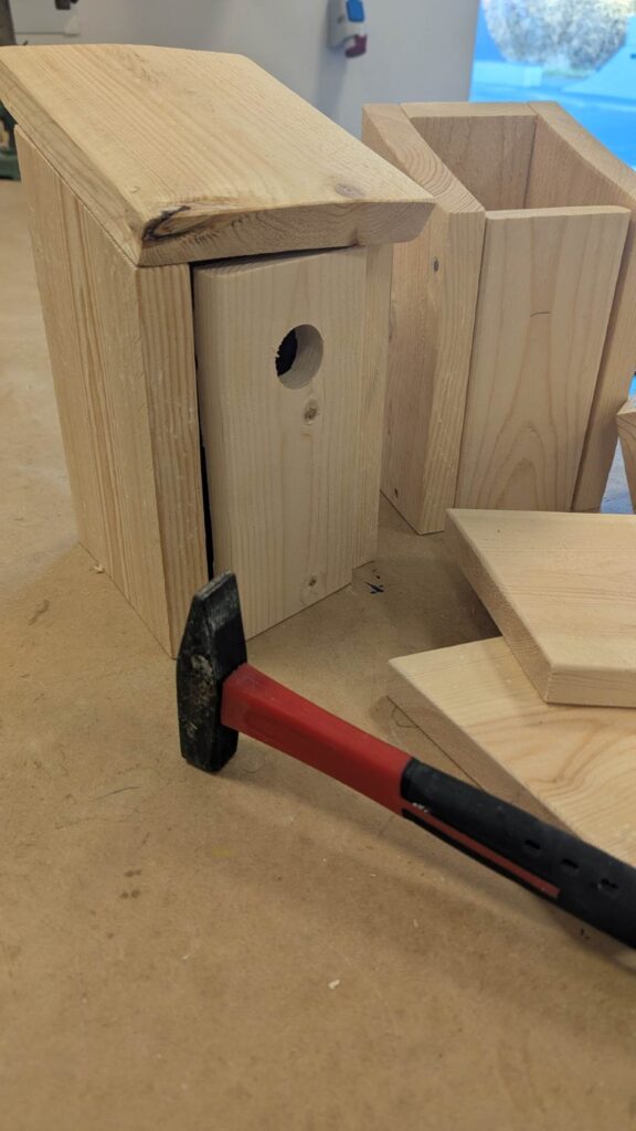 Sider, bund, tag og hammer er vist som dele til at samle dit eget fuglehus.